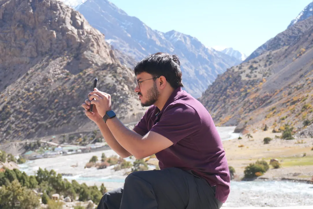 Nitin Raturi photographing a sunny mountain river valley on a phone
